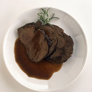 Plate of Manzo al Barolo, slices of marinated beef in red wine sauce, garnished with sprig of rosemary, a typical dish from Piedmont, Italy, view from above