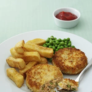 Plate of salmon fishcakes, chips and peas, and a bowl of tomato ketchup, close-up