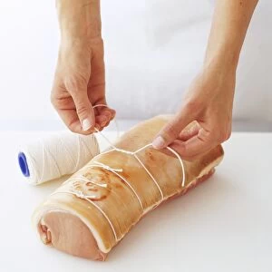 Pork loin rolled into a loaf shape being tied with kitchen string