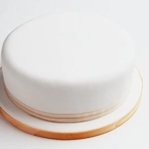 Round fruit cake covered in marzipan and smooth, pure white sugarpaste icing, ribbon decorating cake and board, high angle view