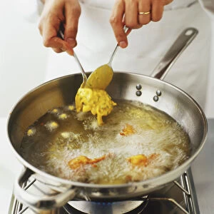 Using two spoons to drop small portions of onion-batter mixture into hot oil in a frying pan
