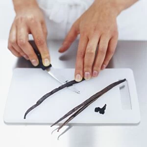Vanilla pods being split with a knife on chopping board