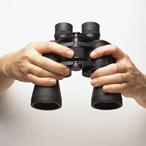 Hands holding binoculars, finger turning central knob, adjusting focus