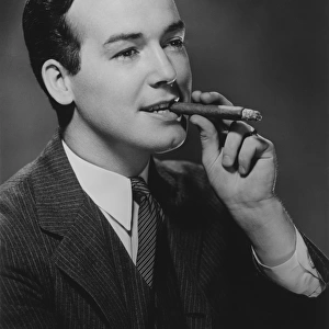 Man smoking cigar in studio, (B&W), portrait