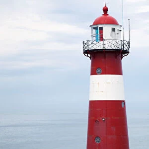 Red and white lighthouse along the coast with a sailboat in the distance near westkapelle; Zealand, netherlands