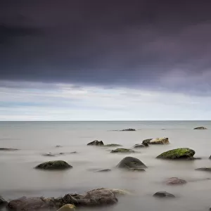 Rocks in tranquil water under storm clouds; Northumberland england