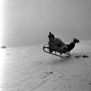 Fun riding a sledge downhill on in the snow on the slopes of Lyme Park in Disley Cheshire