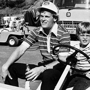Golfer Johnny Miller holding a bottle of water sitting in electric golf buggy with his