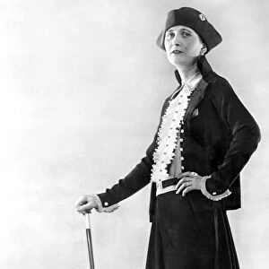 Woman wearing black jacket with skirt and long drape coat over with matching black hat