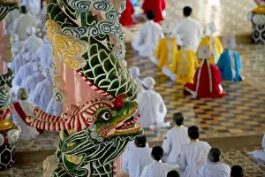: Caodaist disciples sitting beside colourful columns with dragons during ceremony