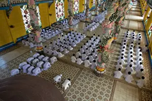 : Caodaist disciples sitting beside colourful columns with dragons during ceremony