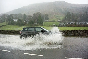 Flood Prints: Car driving through floodwater on road during heavy rainfall