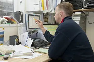 Jobs Prints: Dairy farming, farmer looking at computer in farm office, England, November