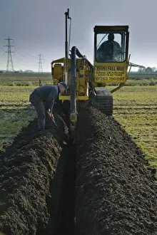 Field drainage, continuous pipe laying machine working in arable field, Pilling, Lancashire, England, march
