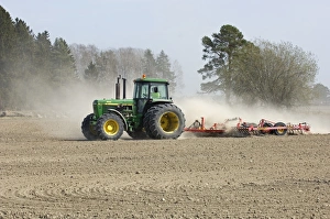 John Deere tractor pulling harrows, harrowing field with wind blown dust, Sweden, spring