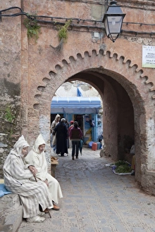 Local Prints: Men wearing djellaba sitting beside medina archway in city, Chefchaouen, Morocco, april