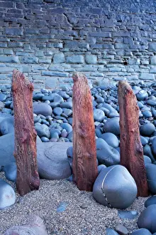 Defence Prints: Remains of old sea defences emerge from shingle and pebbles in front of modern sea wall on beach