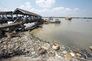 Pollution Prints: Rubbish at edge of river with jetty and boats, Yangon, Myanmar, March