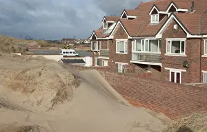 Encroaches Prints: Sand blown from beach forming dunes building up against garden wall next to houses in seaside resort town
