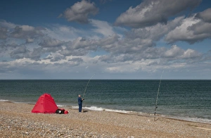 Shingle Prints: Sea angler fishing beside shelter on shingle beach, Cley, Norfolk, England, september