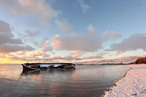 Ship Prints: Snow covered riverbank and wreck of old barge partly submerged by incoming tidal river at sunset