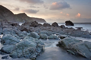 Cliff Prints: Stream flowing through rocks on beach at sunset