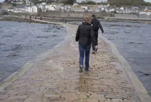Pathway Prints: Tourists walking in seawater covering manmade causeway from tidal island, St