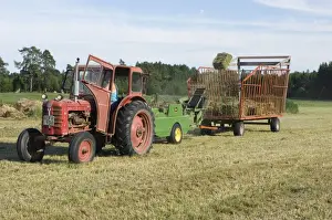 Tractor baling hay crop, baler tossing small bales into wagon, Sweden