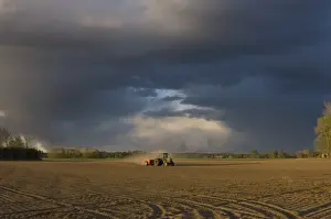 Tractor drilling arable field, with approaching storm clouds, Sweden