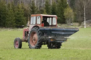 Tractor with fertilizer spreader, spreading nitrogen granular fertilizer on field, Sweden, may
