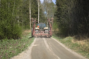 Tractor with harrow, driving along road in woodland, Sweden