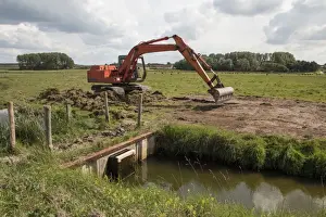 Using a digger for maintenance work on sluice gate at Deepdale Marsh north Norfolk