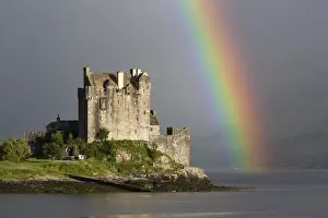 View of restored castle on tidal island in sea loch with rainbow, in evening sunlight, Eilean Donan Castle, Loch Duich