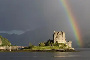 View of restored castle on tidal island in sea loch with rainbow, in evening sunlight, Eilean Donan Castle, Loch Duich