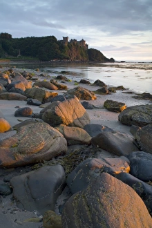 Trending: View of rocks on beach and clifftop castle at sunset