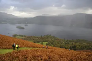 Slopes Prints: View of walkers descending through bracken covered fellside towards lake with rain squall overhead