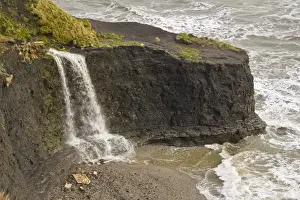 Hard Prints: Waterfall flowing over hard shale to beach on coast with rough sea